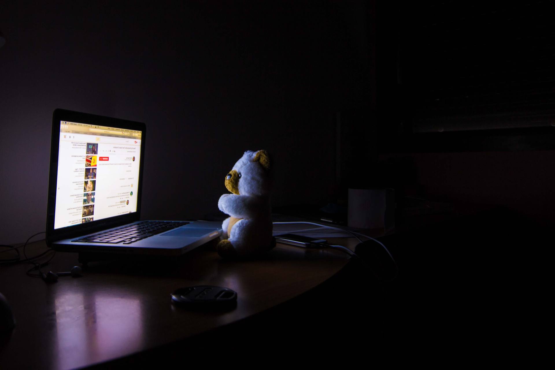 Um ursinho de pelúcia sentado em frente ao computador em um ambiente escuro.