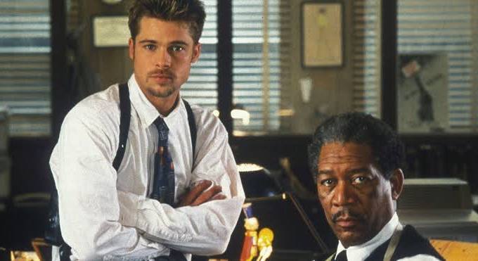 Dois atores: Morgan Freeman e Brad Pitt, olhando para a câmera num cenário policial. Filme: “Seven - Os Sete Pecados Capitais”. 