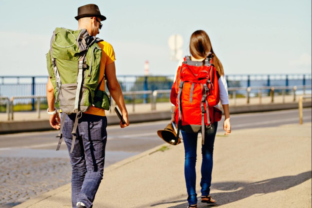 Duas pessoas viajando juntas com mochilas grandes, uma vermelha e outra verde, mais conhecidas como mochilão.