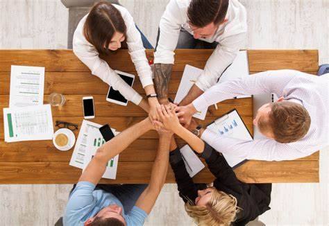 5 pessoas reunidas em ambiente de trabalho dando as mãos