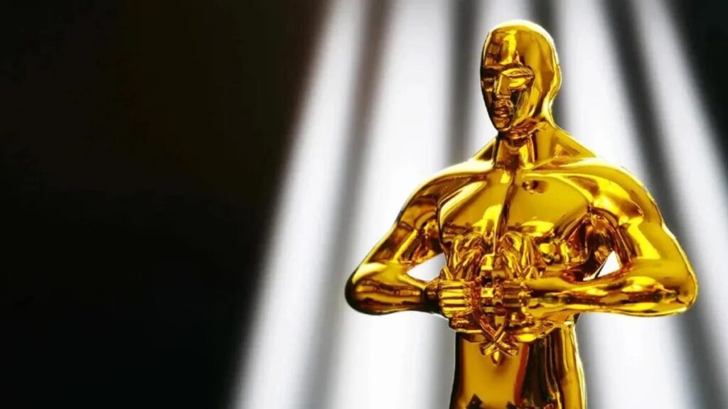 Trofeu do Oscar 2023 com holofotes brancos ao fundo.